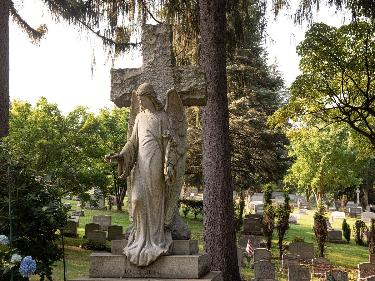 Sculpted headstone of a cross with an angel with open arms